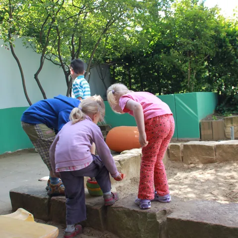 Zwei Kinder beugen sich über die Mauer des Sandkastens und graben im Sand.