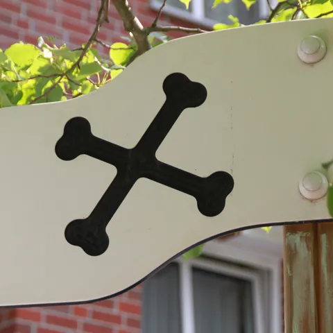 Weißes Schild mit schwarzem Knochensymbol am Zaun des Außengeländes.