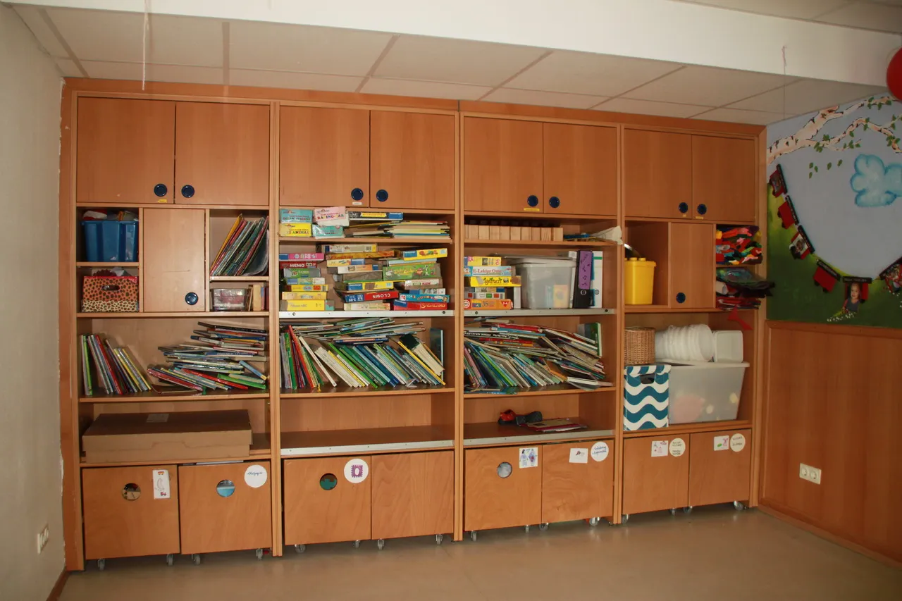 Regal mit Bilderbüchern und beschrifteten Materialkisten, darüber ein selbst gemaltes Wandbild.