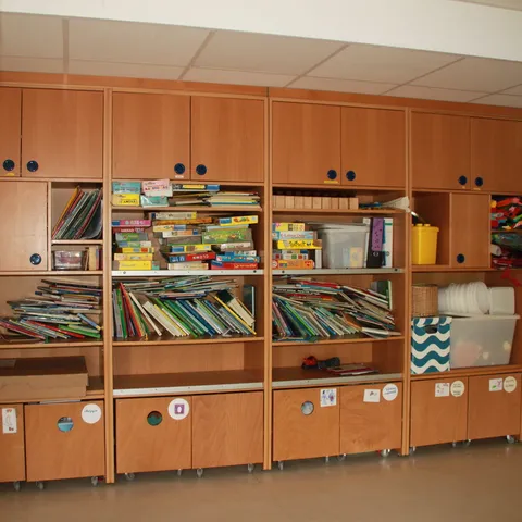 Regal mit Bilderbüchern und beschrifteten Materialkisten, darüber ein selbst gemaltes Wandbild.