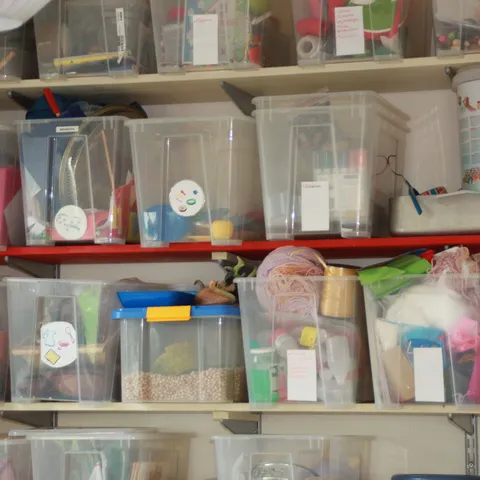 Hohes Regal mit durchsichtigen Materialkisten voller Bastel- und Spielsachen.