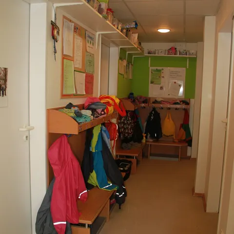 Garderobe mit Kinderjacken an Haken und einer Sitzbank davor.