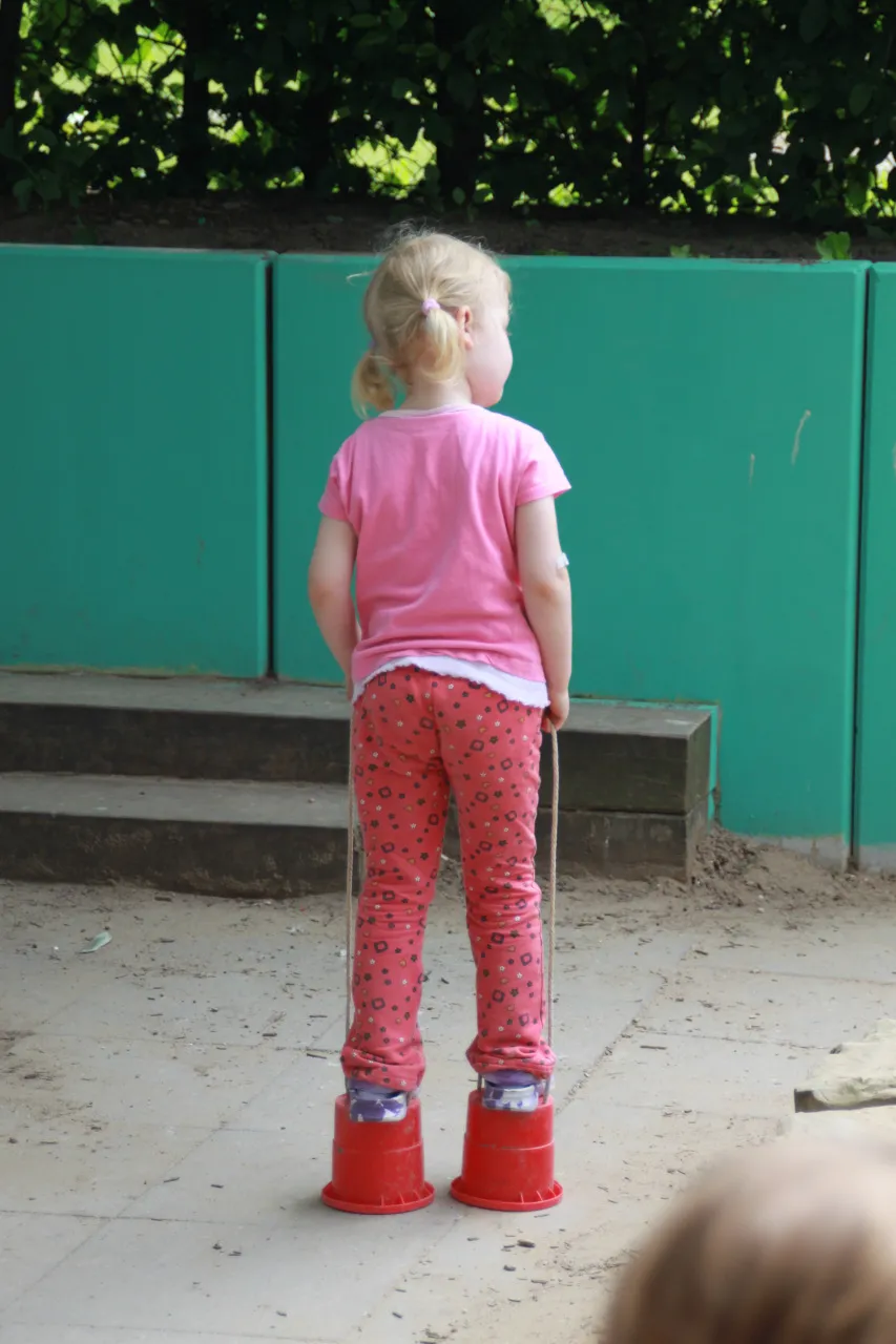 Ein Kind in rosa Kleidung steht vor der grünen Wand des Außengeländes.