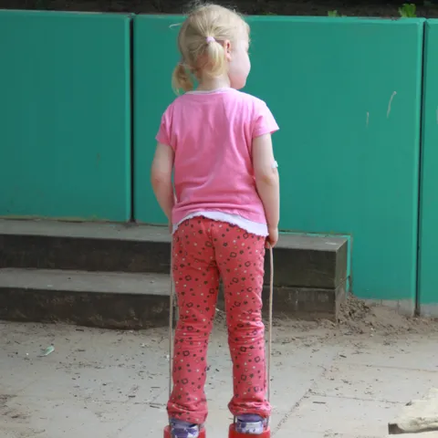 Ein Kind in rosa Kleidung steht vor der grünen Wand des Außengeländes.