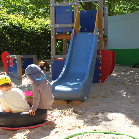 Kinder spielen im Sandkasten, dahinter eine blaue Rutsche und ein Klettergerüst.