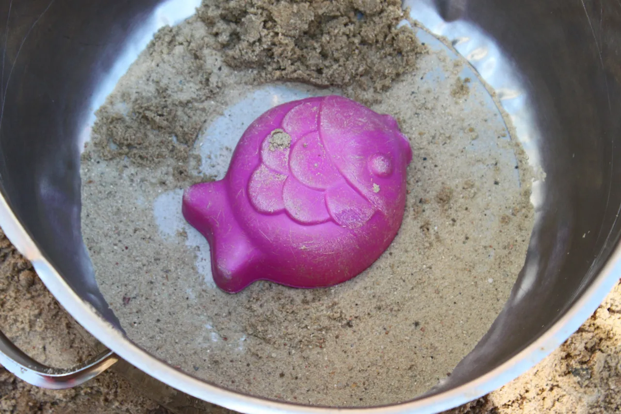 Eine rosa Fischform liegt in einem Metalltopf voller Sand.