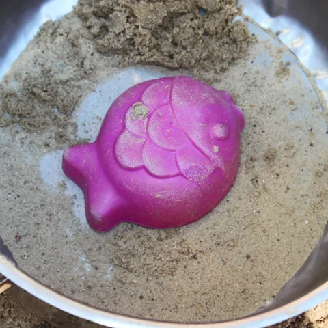 Eine rosa Fischform liegt in einem Metalltopf voller Sand.