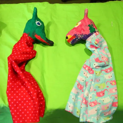 Zwei selbst genähte Handpuppen mit Pferdeköpfen liegen auf einem grünen Tuch.