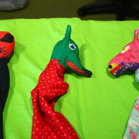 Drei genähte Handpuppen mit Tierköpfen nebeneinander auf grünem Tuch.