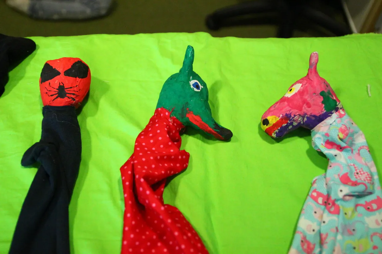 Drei genähte Handpuppen mit Tierköpfen nebeneinander auf grünem Tuch.
