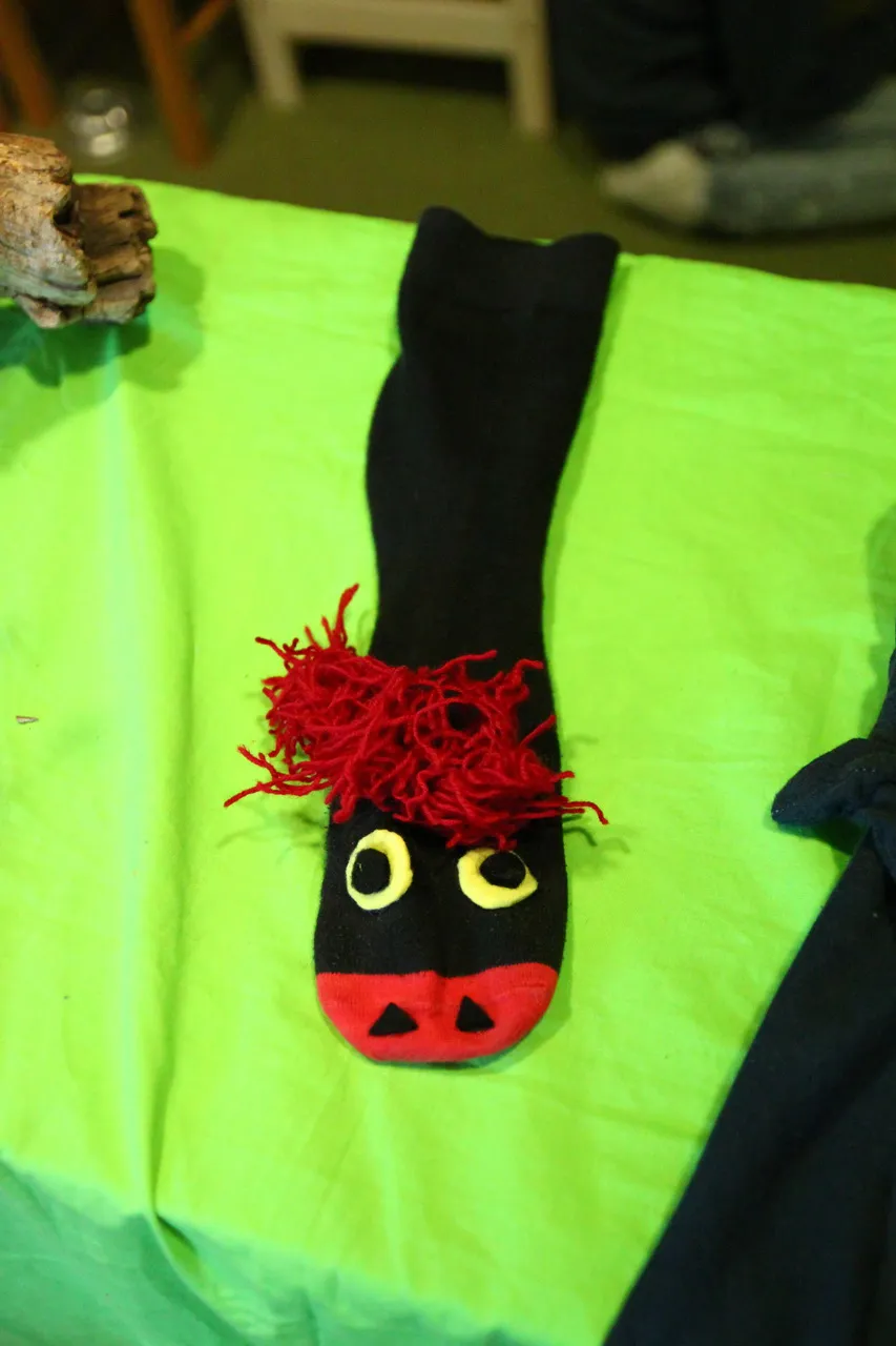 Handpuppe aus einer schwarzen Socke mit gelben Augen und rotem Wollhaar.
