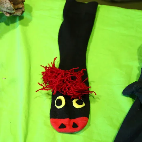 Handpuppe aus einer schwarzen Socke mit gelben Augen und rotem Wollhaar.