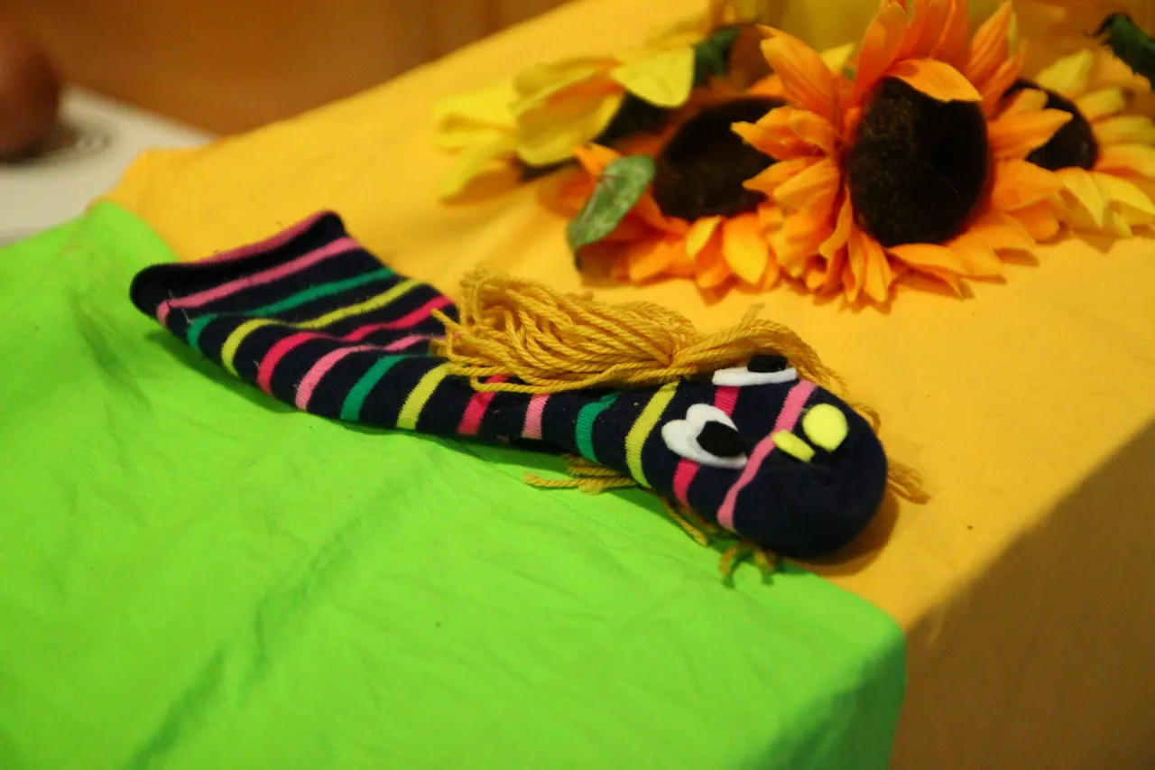 Handpuppe aus einer geringelten Socke, daneben gebastelte Sonnenblumen aus Papier.