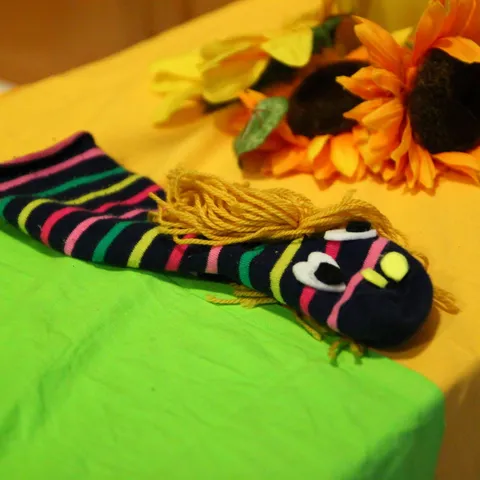 Handpuppe aus einer geringelten Socke, daneben gebastelte Sonnenblumen aus Papier.