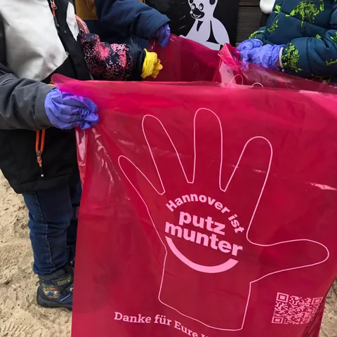 Ein Kind hält einen rosa Müllsack der Aktion „Hannover ist putzmunter“ auf.