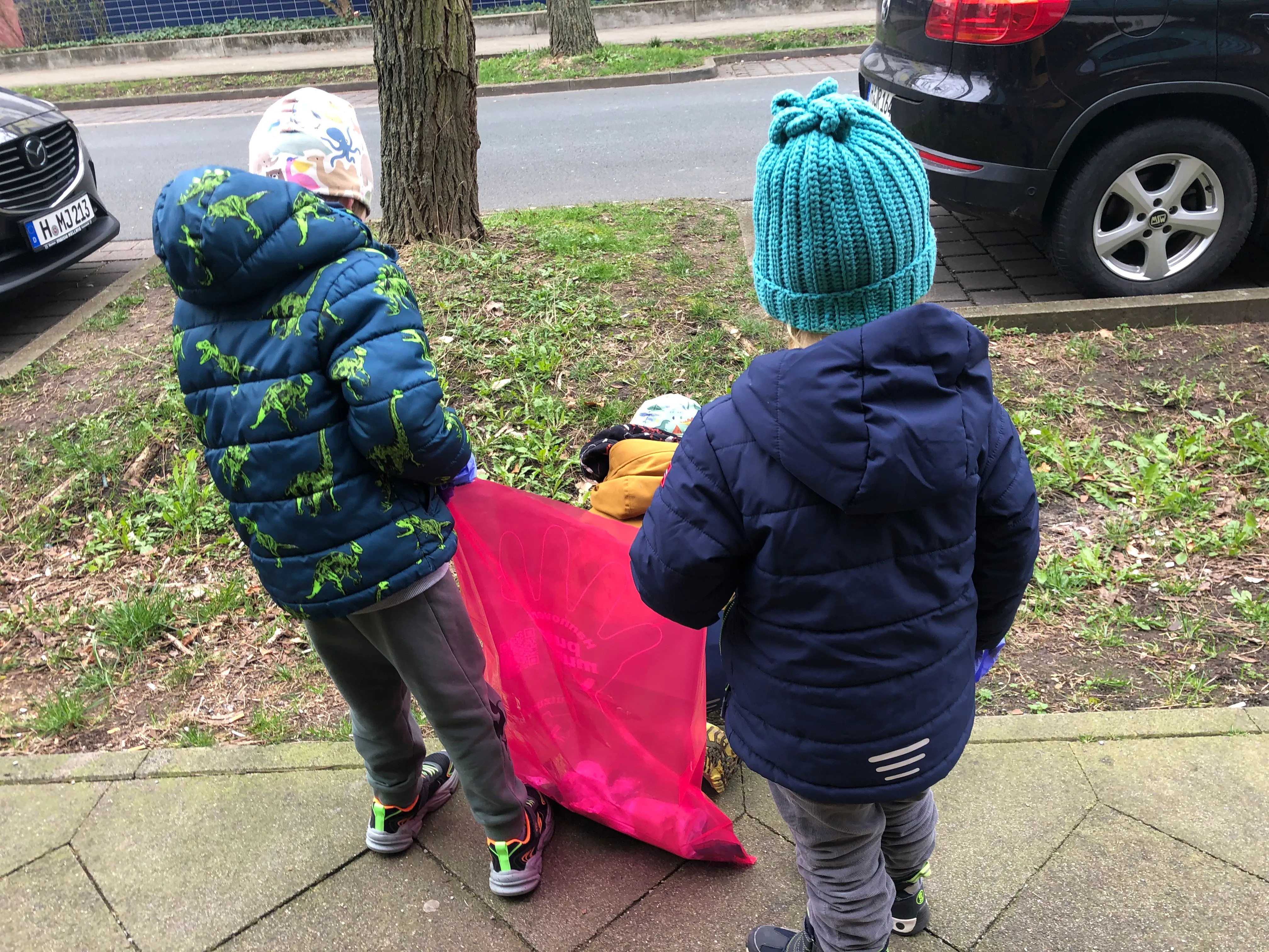 Zwei Kinder tragen gemeinsam einen rosa Müllsack über den Gehweg.