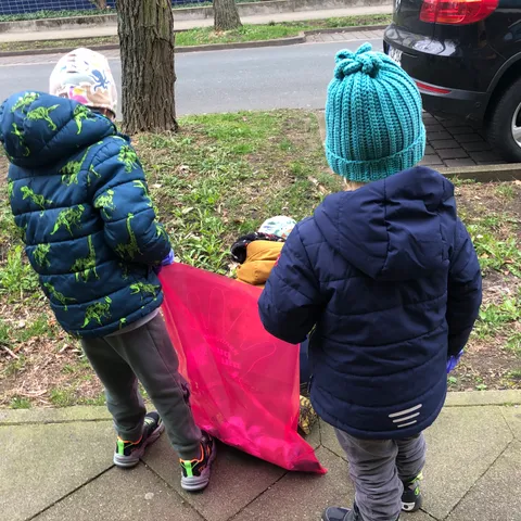 Zwei Kinder tragen gemeinsam einen rosa Müllsack über den Gehweg.