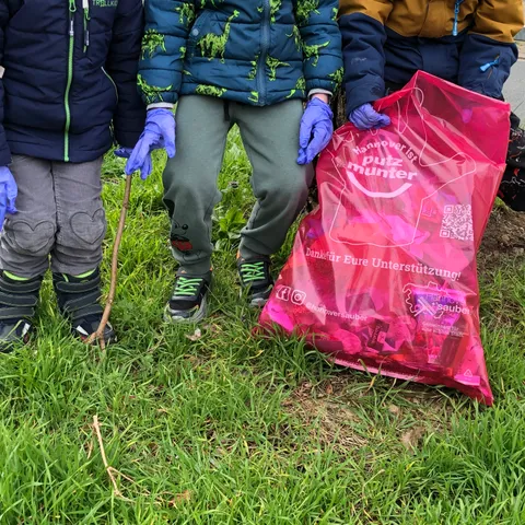 Mehrere Kinder mit Handschuhen sammeln Müll in einen rosa Sack.