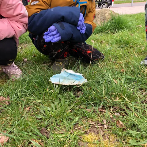 Kinder heben mit behandschuhten Händen Müll aus dem Gras.