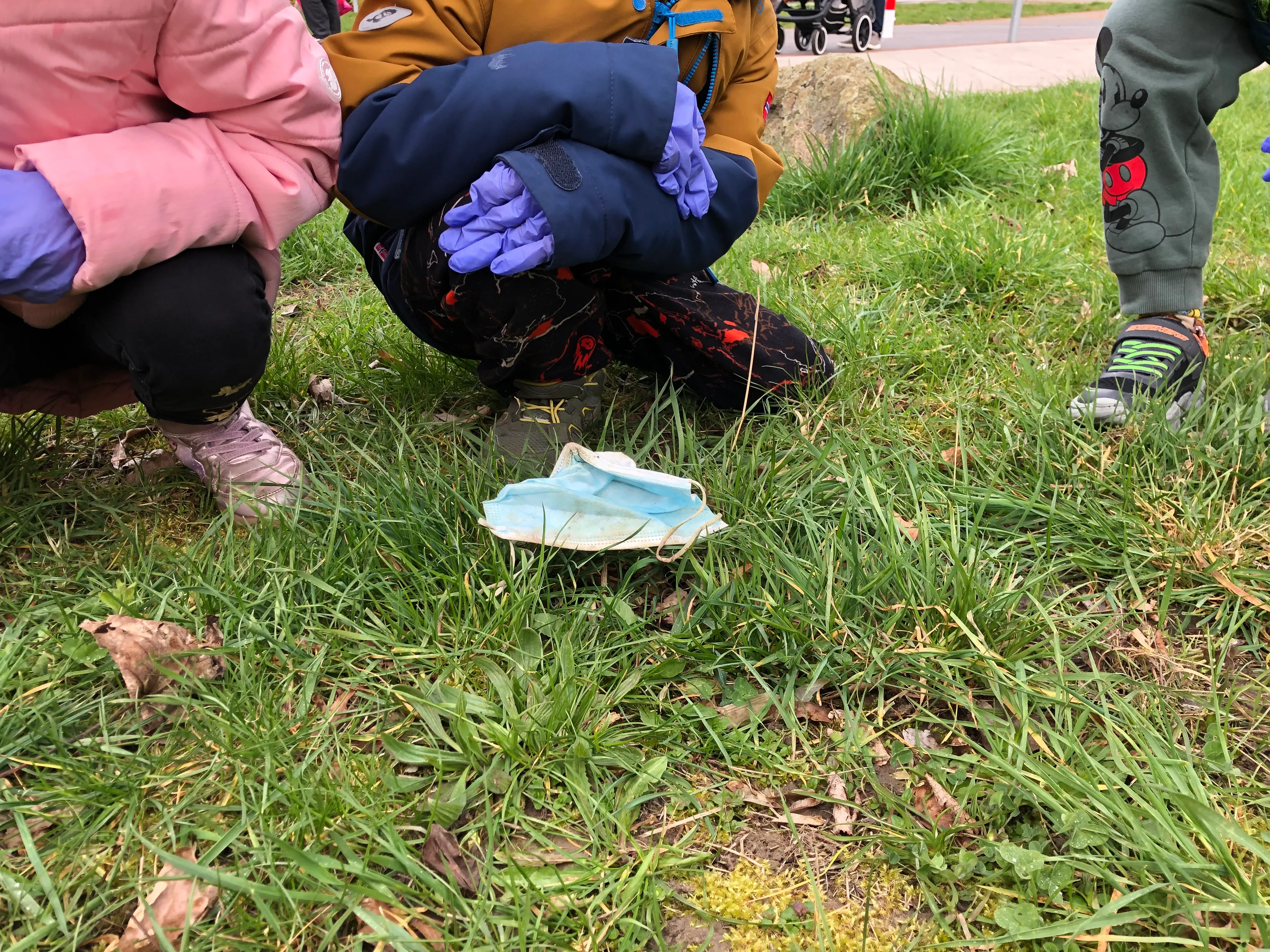 Kinder heben mit behandschuhten Händen Müll aus dem Gras.