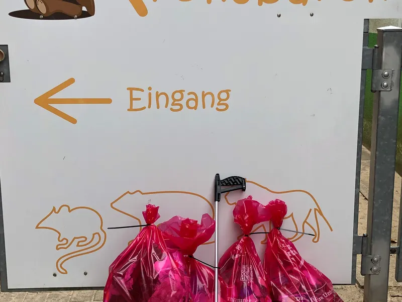 Vier prall gefüllte rosa Müllsäcke und ein Müllgreifer lehnen am Eingangsschild des Kinderladens Kronsbären.