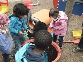 Kinder bepflanzen gemeinsam einen Blumenkübel im Außengelände.